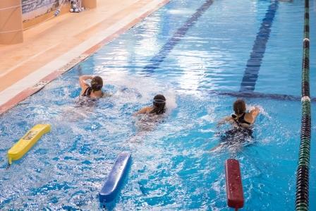 Three lifeguards-in-training swimming with lifeguard floatation device in tow.